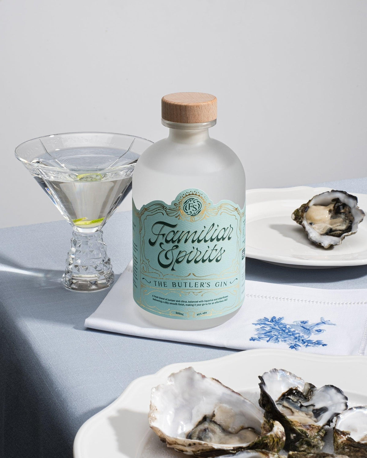 A bottle of gin sitting next to a martini with a plate of oysters in the foreground.