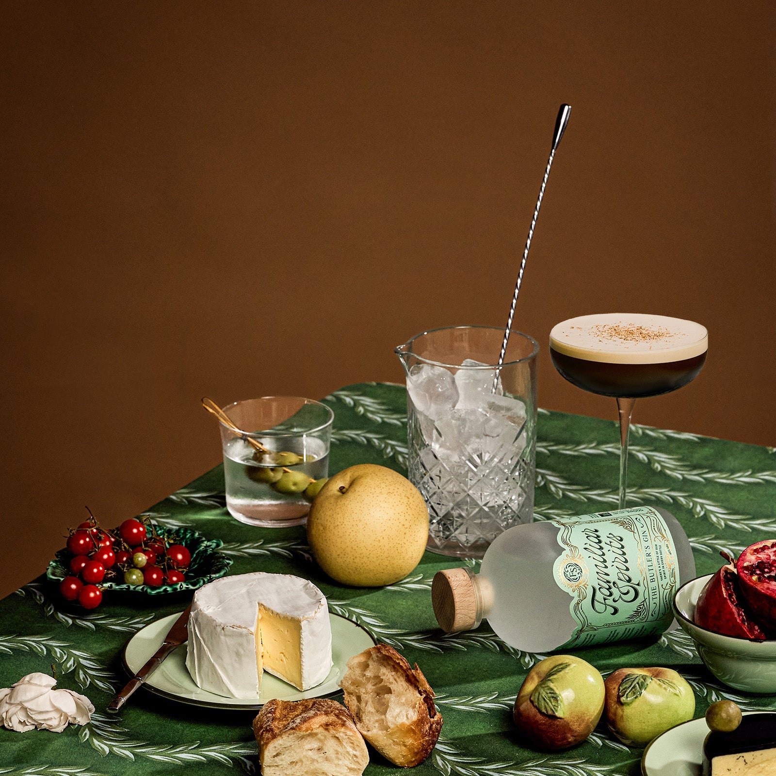 A table set with two cocktails, cheese, bread and fruit on a green tablecloth