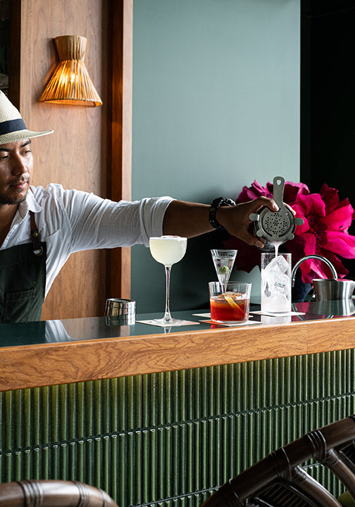 a bartender pouring a cocktail at a green bar