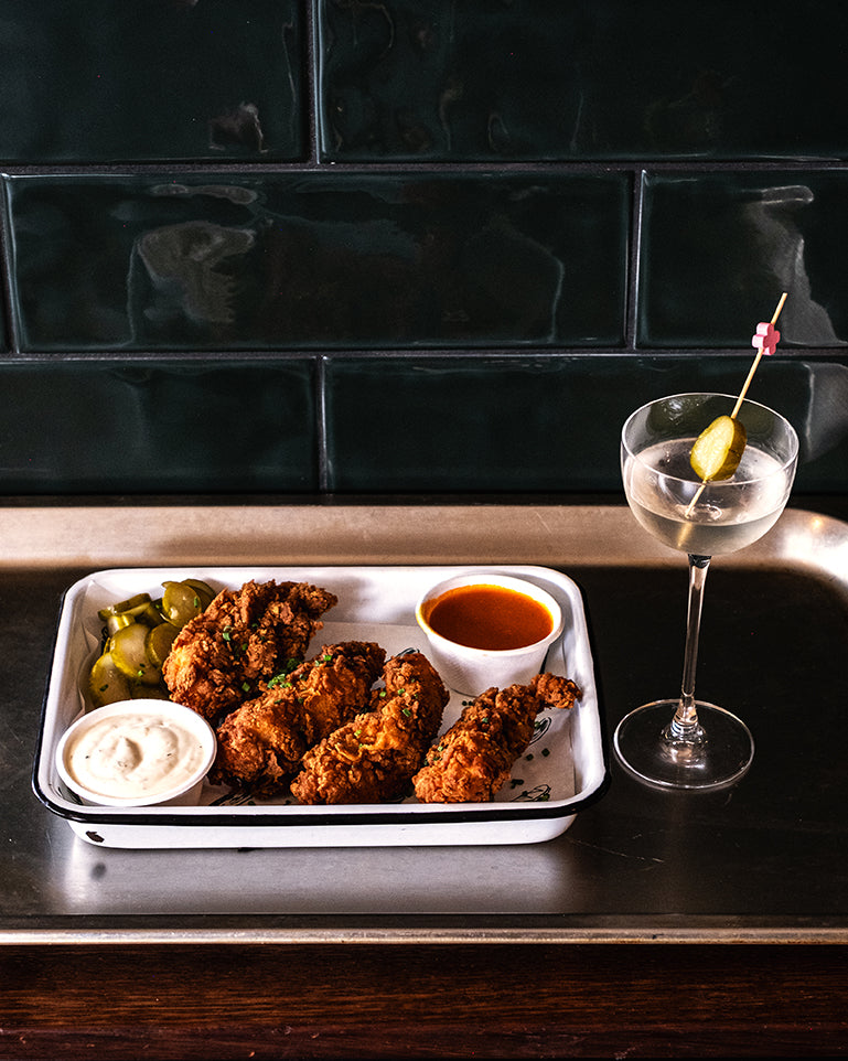 fried chicken tenders, pickles and sauces  on a tray with a martini to the right of it