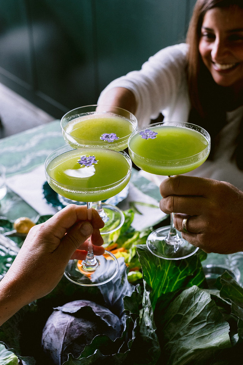 three green basil smash cocktails being 'cheersed' by friends